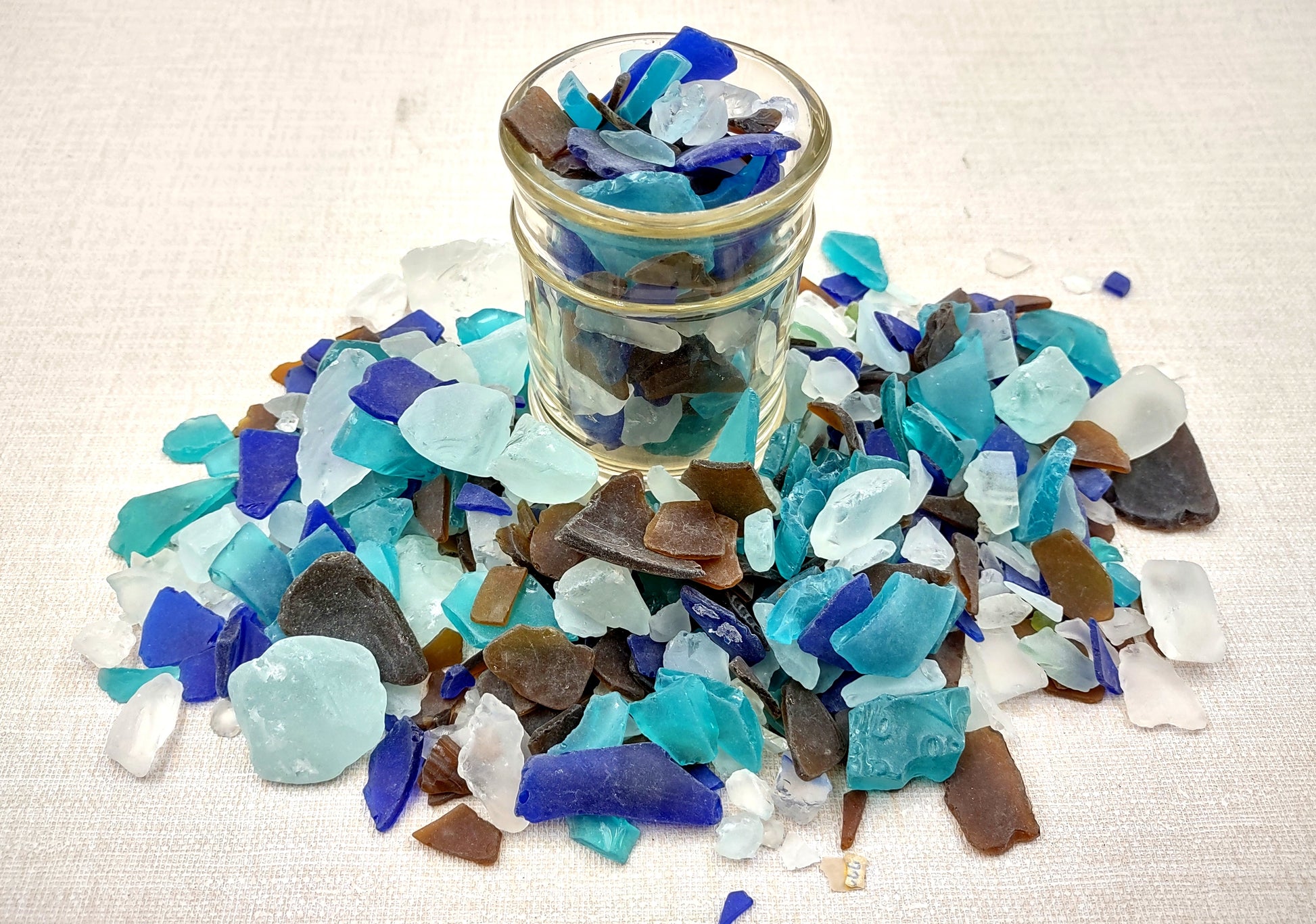 Beach Glass - Medium Tumbled Rough Brown, White & Blue Pacific Assorted - (approx. 1 Kilogram/2.2 lbs. .5-1.25 inches). Multiple blue, white, and brown fragments in a pile. All different shapes and sizes. Copyright 2024 SeaShellSupply.com.