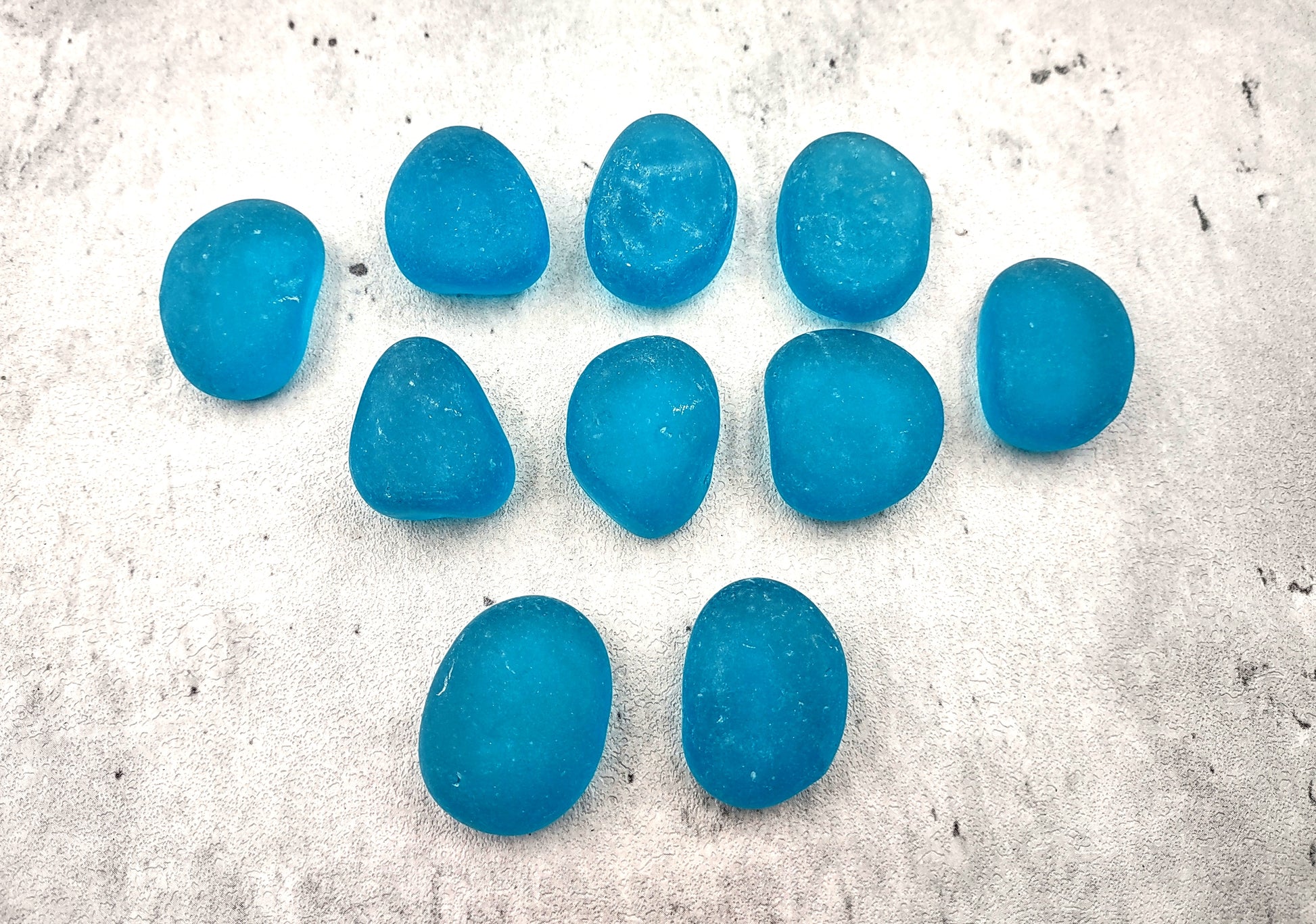 Beach Glass - Rounded Aqua Blue Pebbles - (approx. 1 Kilogram/2.2 lbs. 1-1.5 inches). Multiple smooth blue glass pebbles in a pile. Copyright 2024 SeaShellSupply.com.