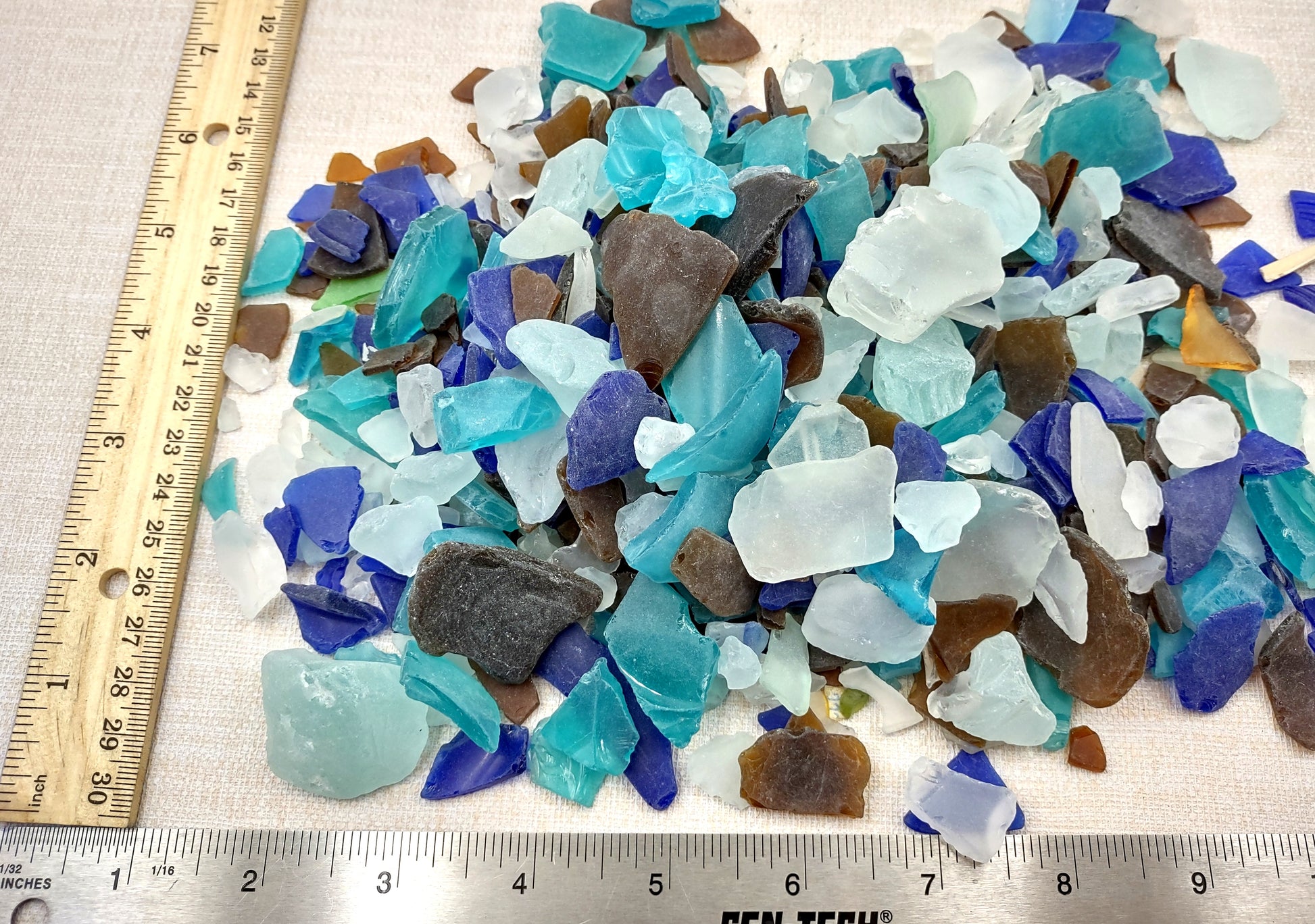 Beach Glass - Medium Tumbled Rough Brown, White & Blue Pacific Assorted - (approx. 1 Kilogram/2.2 lbs. .5-1.25 inches). Multiple blue, white, and brown fragments in a pile. All different shapes and sizes. Copyright 2024 SeaShellSupply.com.