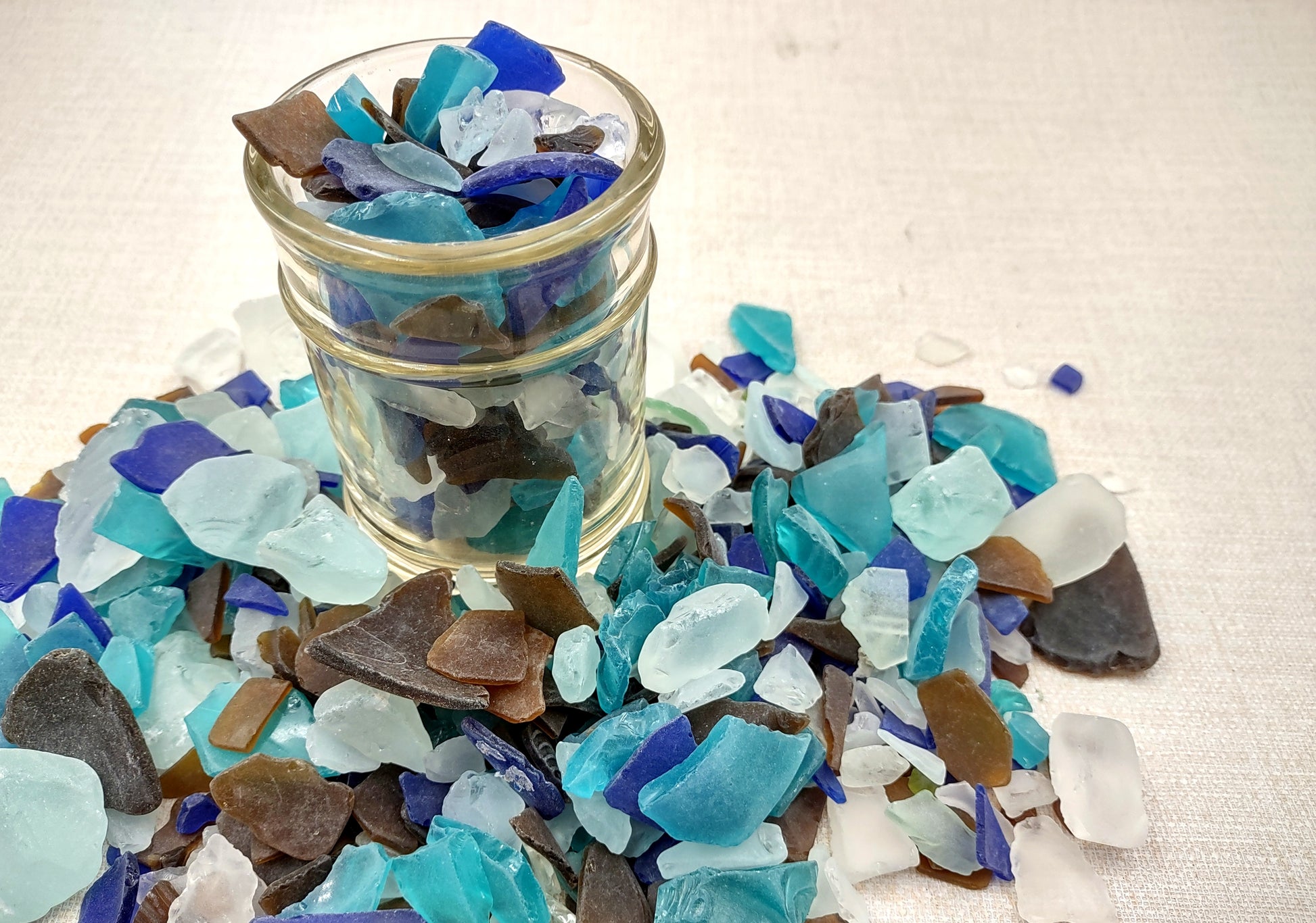 Beach Glass - Medium Tumbled Rough Brown, White & Blue Pacific Assorted - (approx. 1 Kilogram/2.2 lbs. .5-1.25 inches). Multiple blue, white, and brown fragments in a pile. All different shapes and sizes. Copyright 2024 SeaShellSupply.com.