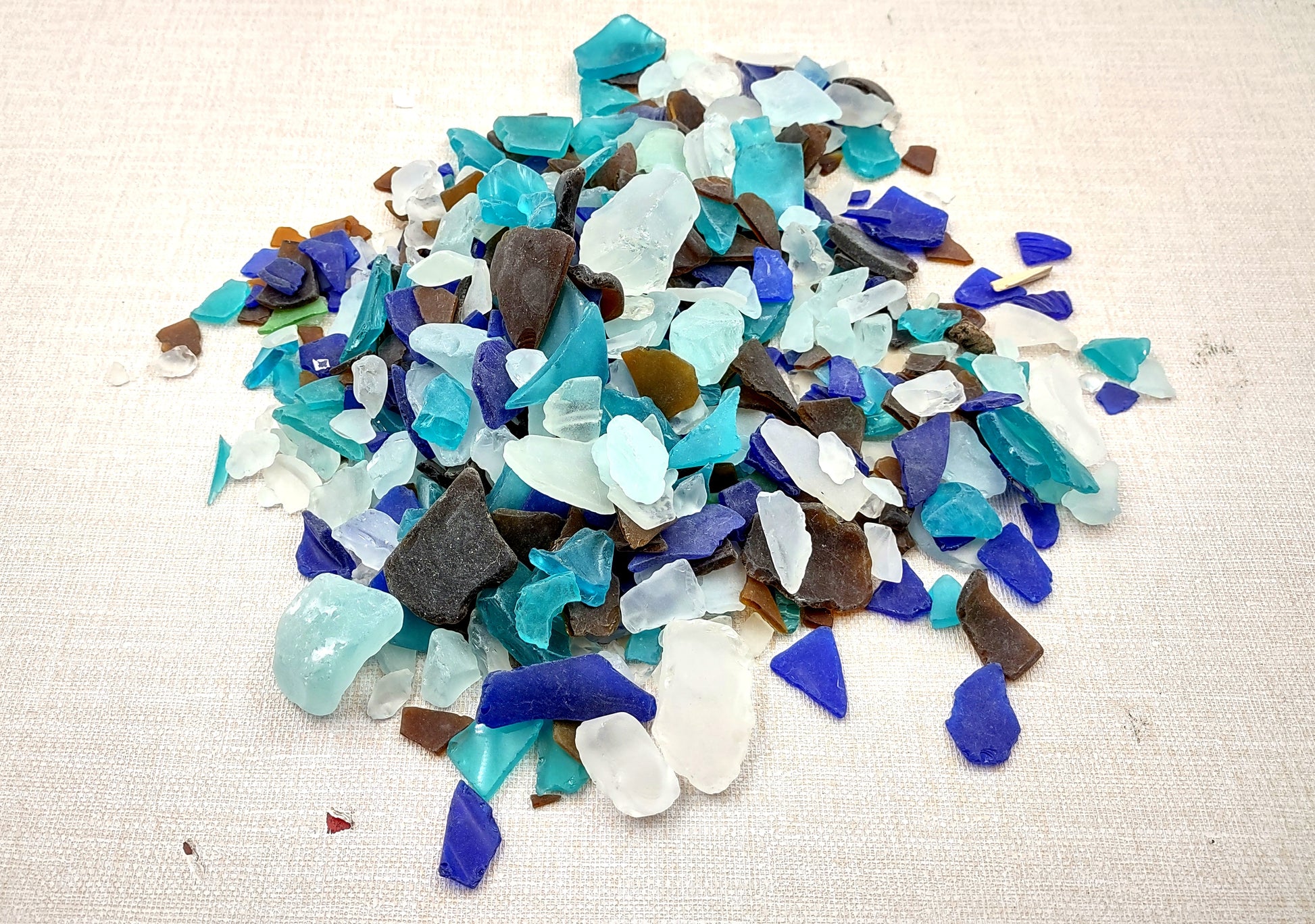 Beach Glass - Medium Tumbled Rough Brown, White & Blue Pacific Assorted - (approx. 1 Kilogram/2.2 lbs. .5-1.25 inches). Multiple blue, white, and brown fragments in a pile. All different shapes and sizes. Copyright 2024 SeaShellSupply.com.
