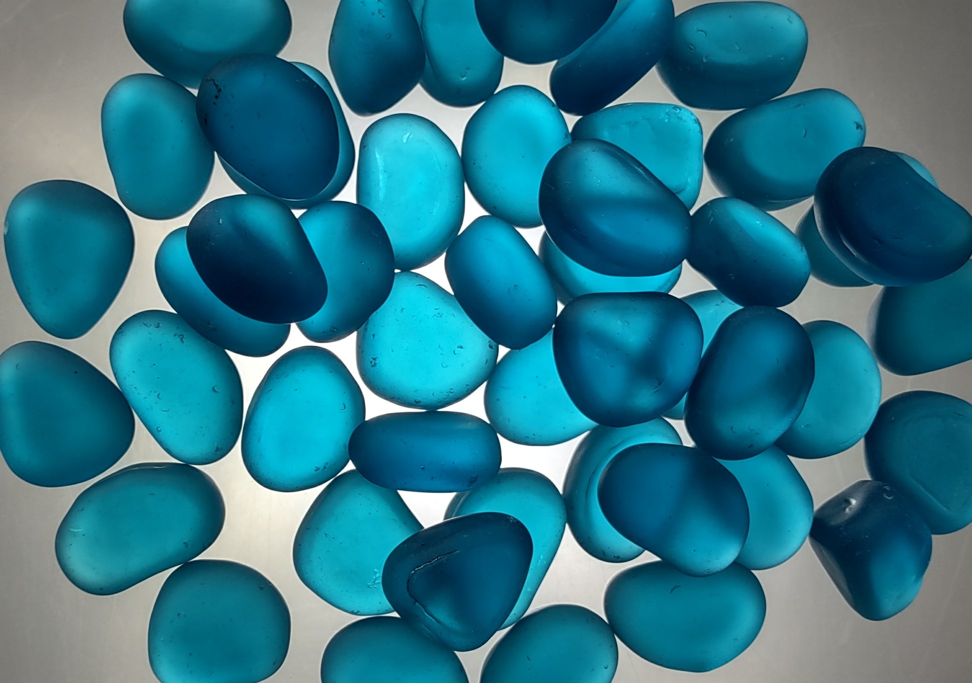 Beach Glass - Rounded Aqua Blue Pebbles - (approx. 1 Kilogram/2.2 lbs. 1-1.5 inches). Multiple smooth blue glass pebbles in a pile. Copyright 2024 SeaShellSupply.com.