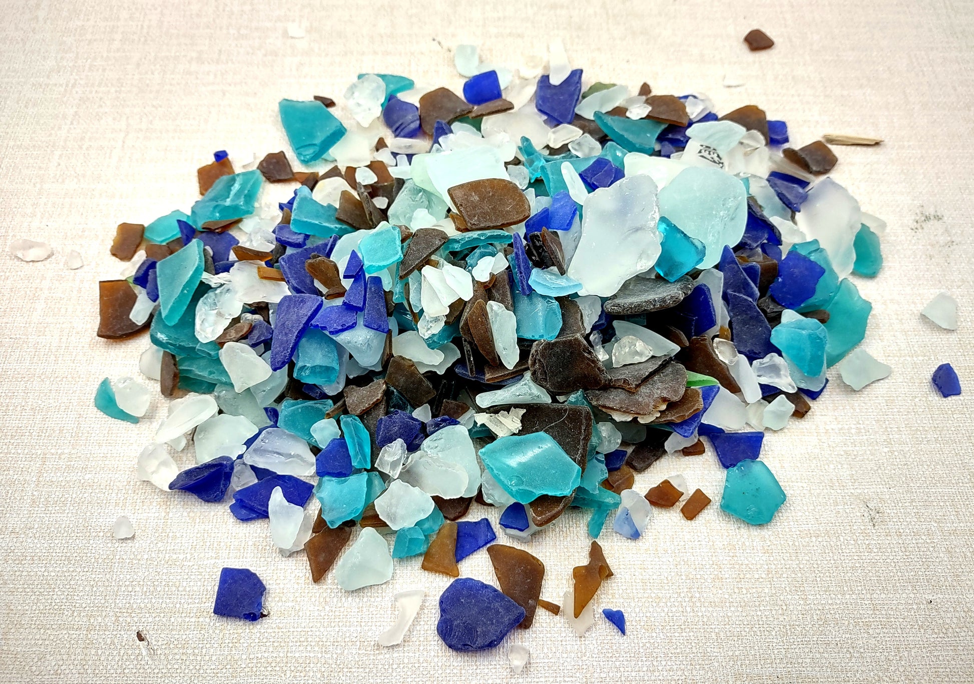Beach Glass - Medium Tumbled Rough Brown, White & Blue Pacific Assorted - (approx. 1 Kilogram/2.2 lbs. .5-1.25 inches). Multiple blue, white, and brown fragments in a pile. All different shapes and sizes. Copyright 2024 SeaShellSupply.com.