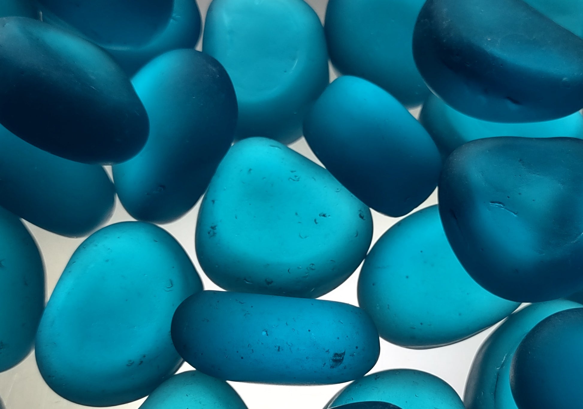 Beach Glass - Rounded Aqua Blue Pebbles - (approx. 1 Kilogram/2.2 lbs. 1-1.5 inches). Multiple smooth blue glass pebbles in a pile. Copyright 2024 SeaShellSupply.com.