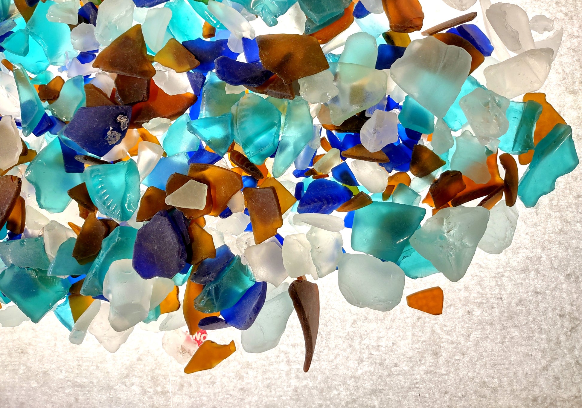 Beach Glass - Medium Tumbled Rough Brown, White & Blue Pacific Assorted - (approx. 1 Kilogram/2.2 lbs. .5-1.25 inches). Multiple blue, white, and brown fragments in a pile. All different shapes and sizes. Copyright 2024 SeaShellSupply.com.
