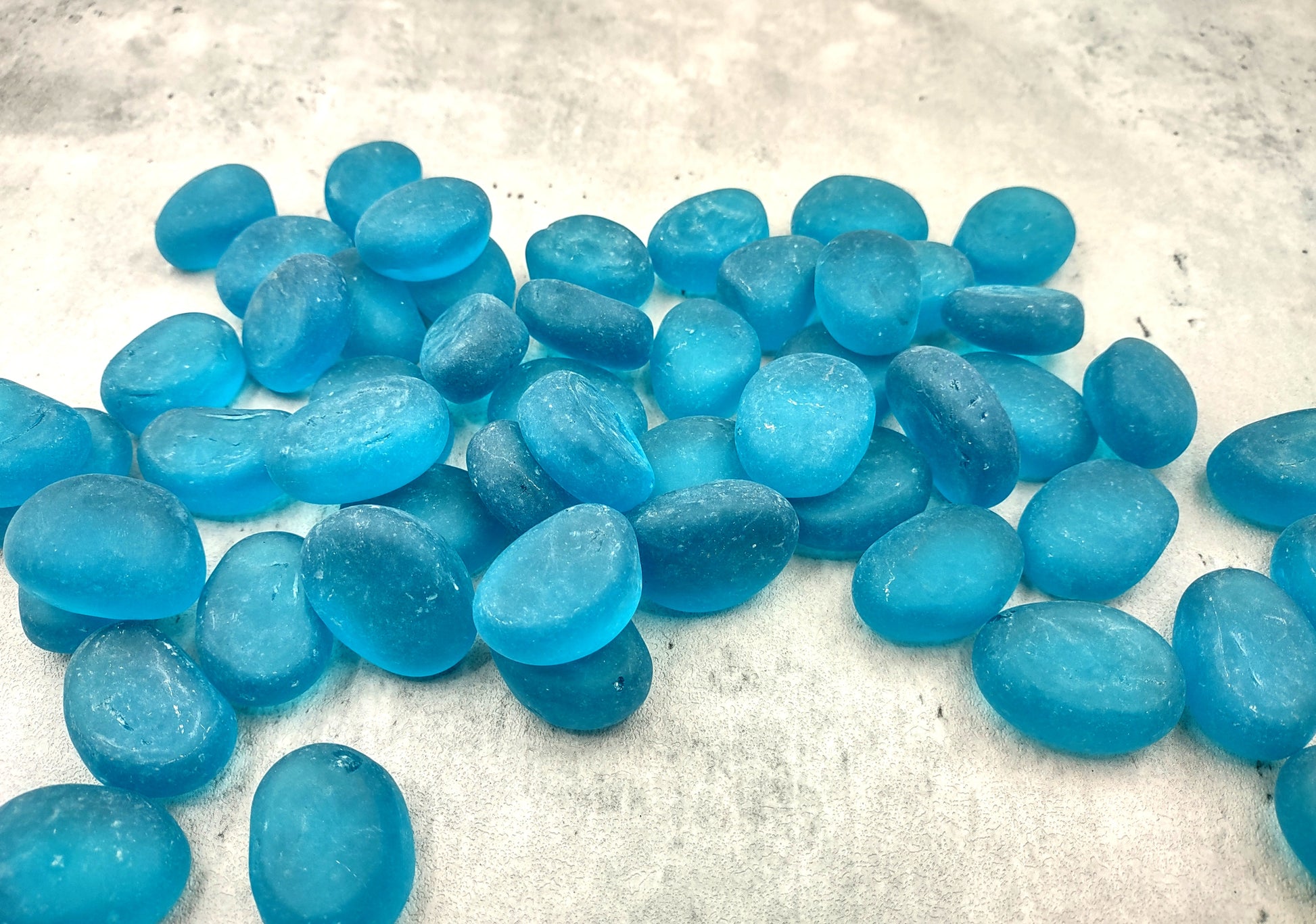 Beach Glass - Rounded Aqua Blue Pebbles - (approx. 1 Kilogram/2.2 lbs. 1-1.5 inches). Multiple smooth blue glass pebbles in a pile. Copyright 2024 SeaShellSupply.com.