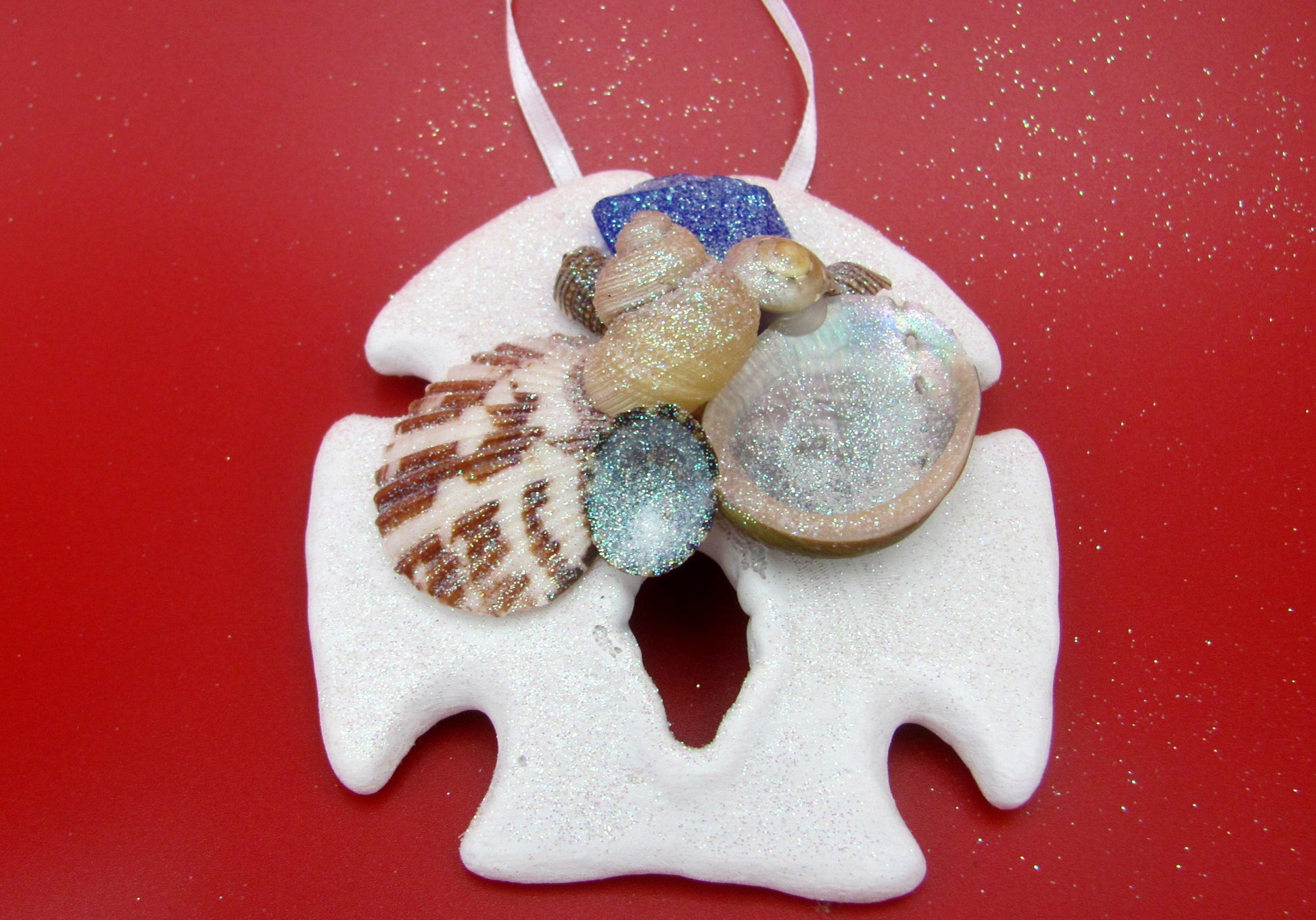 Frosted Blue Sea Glass Sand Dollar Ornament (1 sand dollar approx. 3-5 inches) on red background. Copyright 2022 SeaShellSupply.com.